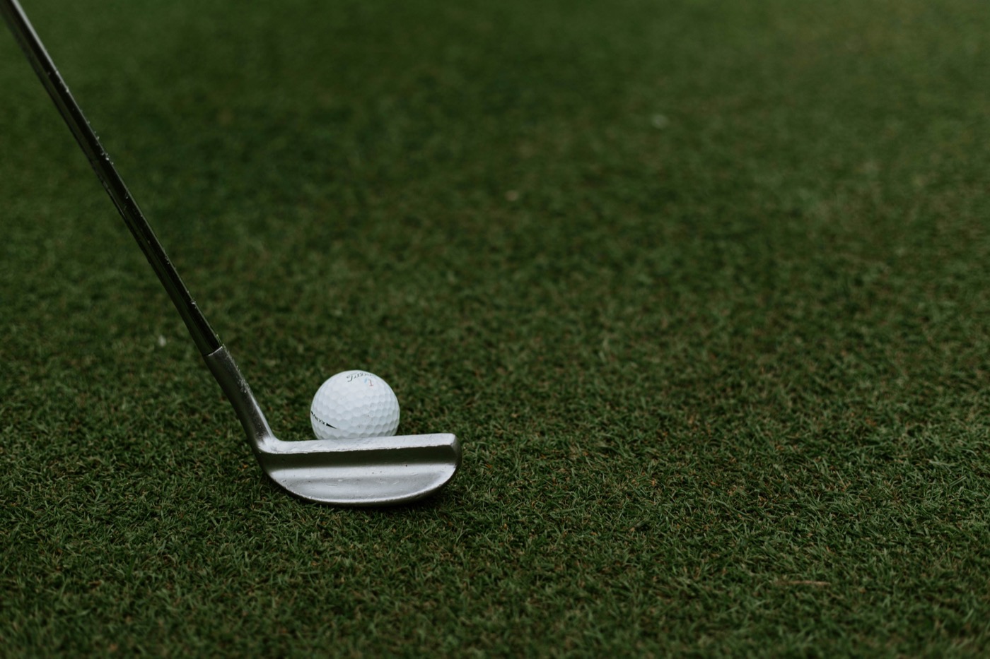 A putter at address behind the ball on a green, captured mid-routine